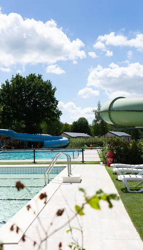 Overzicht van het buitenzwembad met waterglijbanen en ligbedden op de ligweide bij Resort Kaatsheuvel in Noord-Brabant.