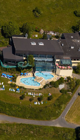 Luchtfoto van het Rhön Park Hotel in Beieren, met het buitenzwembad en de ligweide omgeven door de groene heuvels van de Rhön.