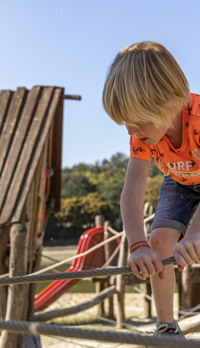 Jongen klimt en klautert vol plezier in de avontuurlijke houten buitenspeeltuin van Vakantiepark Hunzedal in Drenthe.