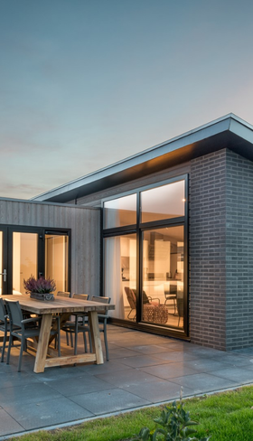 Een luxe, moderne dijklodge op Vakantiepark Zeedijk bij zonsondergang, met een verlicht interieur en een ruim terras in de polder van Zuid-Holland.