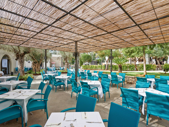 Het gezellige buitenterras van een restaurant bij Protur Safari Park, met een rieten dak en vrolijke turquoise stoelen.