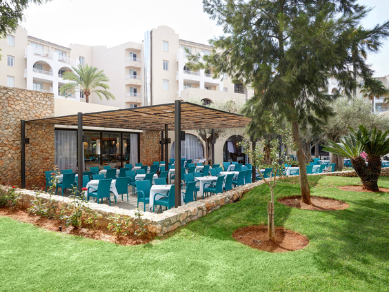 Het buitenterras met turquoise stoelen van een van de restaurants van Protur Safari Park, gelegen aan een groen gazon.
