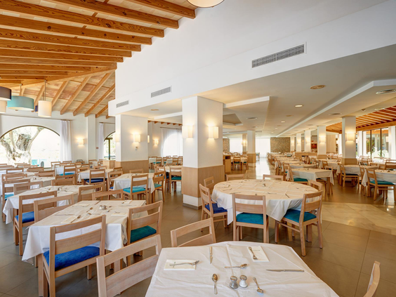 Het interieur van het buffetrestaurant bij Protur Safari Park op Mallorca, met gedekte tafels, houten stoelen en blauwe kussens.