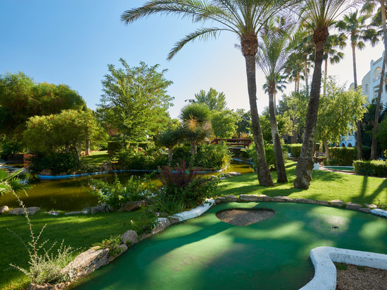 Een hole van de prachtige minigolfbaan bij Protur Safari Park, omgeven door een vijver, groene planten en palmbomen.