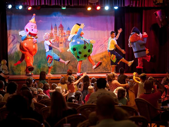 Kinderen dansen en kijken naar een vrolijke theatershow met mascottes en entertainers op het podium bij Aparthotel Royal Son Bou.