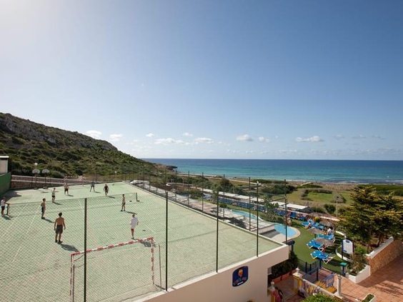 Het multifunctionele sportveld van Royal Son Bou met kinderen die voetballen, gelegen aan de kust met uitzicht op zee op Menorca.