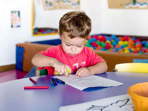 Een jonge, geconcentreerde jongen is aan het kleuren aan een tafel in de kidsclub 'Kikoland' van Aparthotel Royal Son Bou.