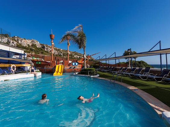 Het grote zwembad bij Aparthotel Royal Son Bou met op de achtergrond het kinderbad met piratenschip en waterglijbaan, gelegen aan de kust van Menorca.