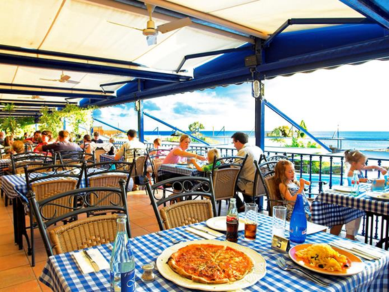 Gasten genieten van een lunch, waaronder pizza, op het sfeervolle buitenterras van het restaurant bij Royal Son Bou, met prachtig uitzicht over de zee.