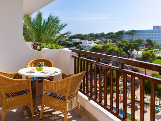 Een balkon met een rotan zitje bij Esmeralda Park, dat een weids uitzicht biedt over het resort en de groene omgeving van Cala d'Or.