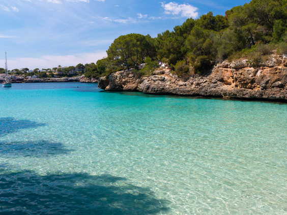 Kristalhelder, turquoise zeewater in een schilderachtige baai bij Cala d'Or op Mallorca, omringd door rotsen.
