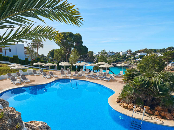 Het grote, lagune-stijl zwembad van Appartementen Esmeralda Park in Cala d'Or, omringd door ligbedjes en palmbomen.