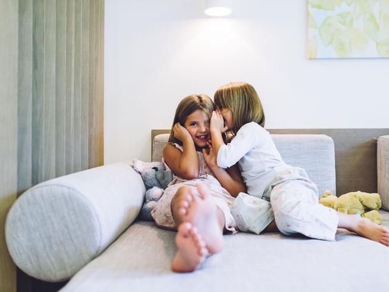 Twee lachende kinderen die geheimpjes fluisteren op de bank in het moderne appartement van Esmeralda Park, Mallorca.