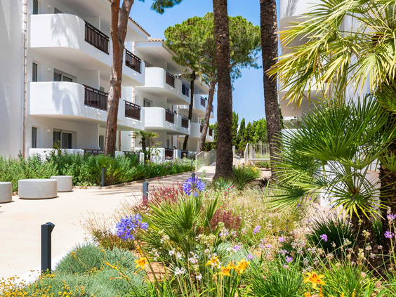 De moderne, witte appartementengebouwen van Esmeralda Park, omgeven door een prachtige, bloemrijke tuin met palmbomen op Mallorca.