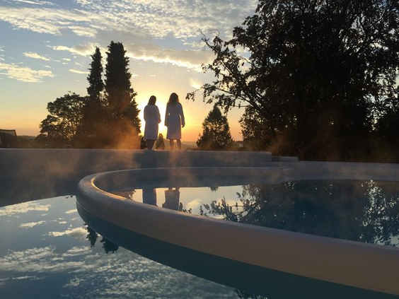 Gasten in badjas genieten van de zonsondergang bij het wellness buitenzwembad van Hotel Atlanta in het Limburgse heuvellandschap