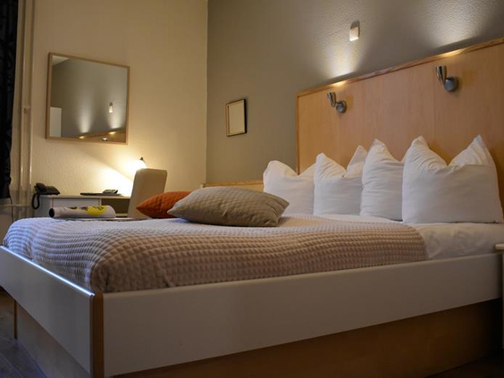Sfeervolle hotelkamer in Hotel Atlanta met een opgemaakt bed met sierkussens en een verlicht bureau op de achtergrond