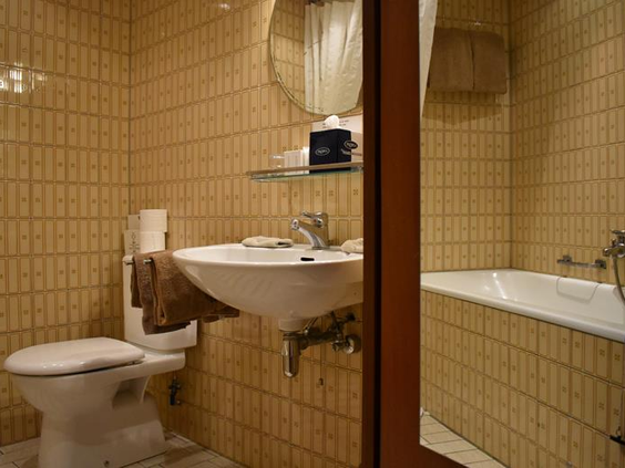 De retro badkamer van Hotel Atlanta in Limburg met beige tegels een toilet een wastafel en een bad