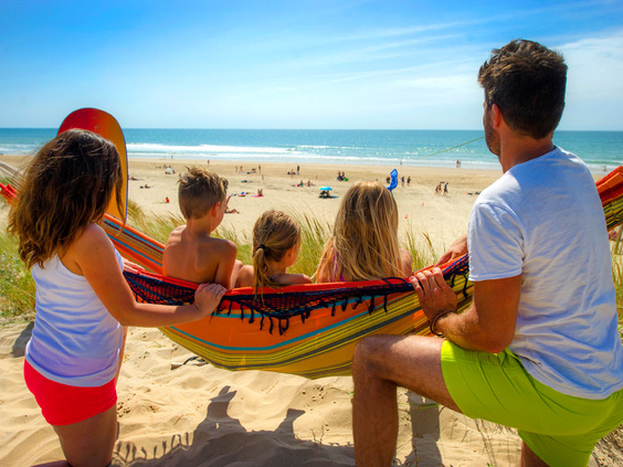 Gezin relaxt samen in een kleurrijke hangmat in de duinen en kijkt uit over het strand en de zee bij Atlantic Club Montalivet.