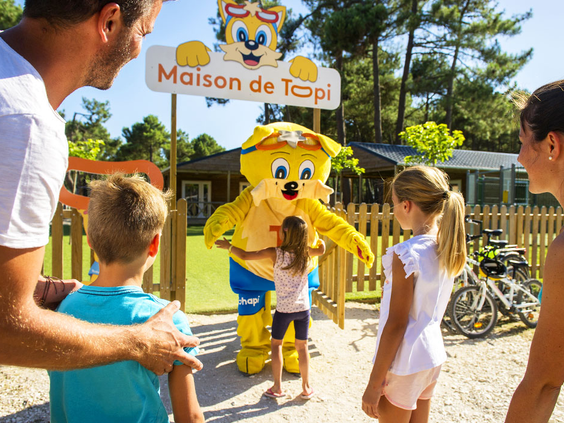Kinderen geven een high five aan de vrolijke campingmascotte Topi bij zijn eigen huisje 'Maison de Topi' op Atlantic Club Montalivet.