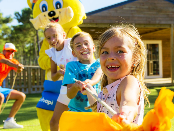 Vrolijke kinderen doen samen met mascotte Topi mee aan een potje touwtrekken tijdens de animatie op camping Atlantic Club Montalivet.