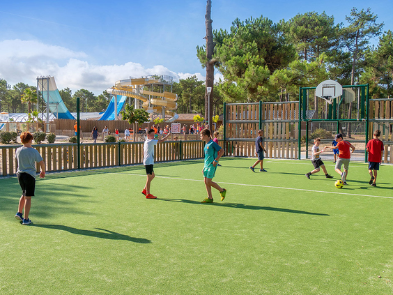 Kinderen spelen een partijtje voetbal op het multifunctionele kunstgras sportveld, omringd door bomen op camping Atlantic Club Montalivet.