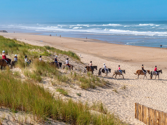 Groep ruiters te paard maakt een tocht door de duinen en langs de branding van de Atlantische Oceaan, vlak bij camping Atlantic Club Montalivet.