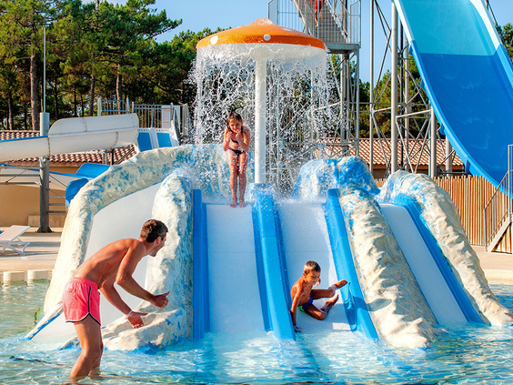 Jonge kinderen glijden van een brede kinderglijbaan met een watervalfontein in het peuterbad van Atlantic Club Montalivet.