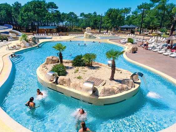 Gasten ontspannen in het lagune-stijl zwembad met een eilandje vol palmbomen op de kindvriendelijke camping Atlantic Club Montalivet.