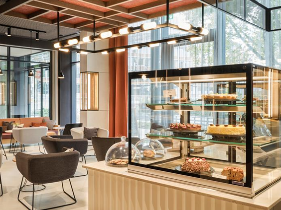 De stijlvolle lounge van het ATLANTIC Hotel Münster, met een vitrine vol heerlijke, huisgemaakte taartjes en gebak.