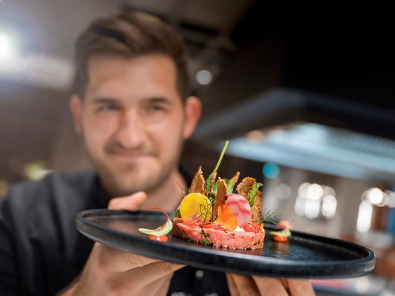 Een chef in het restaurant van het ATLANTIC Hotel Münster presenteert een culinair en kindvriendelijk gerecht.