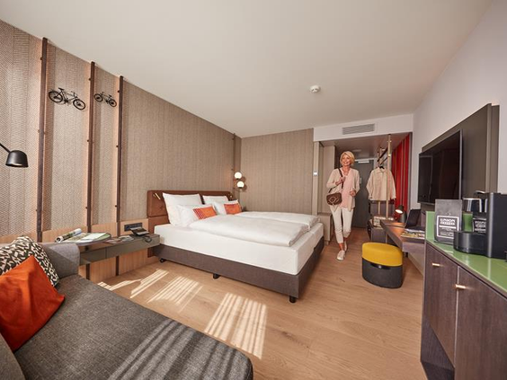 Een ruim en licht ingerichte familiekamer in het ATLANTIC Hotel Münster waar een gezin net arriveert voor hun stedentrip.