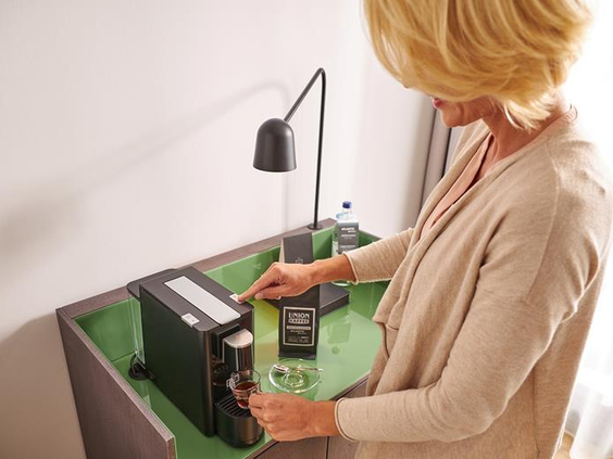 Een gast die een vers kopje koffie zet met het koffiezetapparaat op de luxe hotelkamer van het ATLANTIC Hotel Münster.