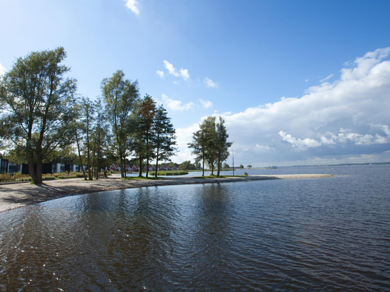 Uitzicht over het kabbelende Veluwemeer vanaf het zandstrand van Vakantiepark Bad Hoophuizen op een zonnige dag.