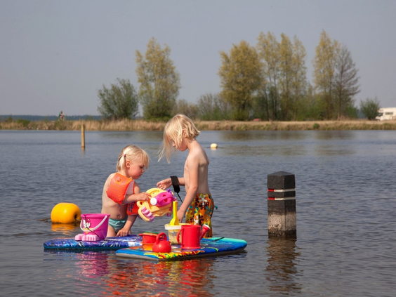 Twee jonge kinderen met zwembandjes spelen veilig met emmertjes en schepjes in het ondiepe water van het Veluwemeer.
