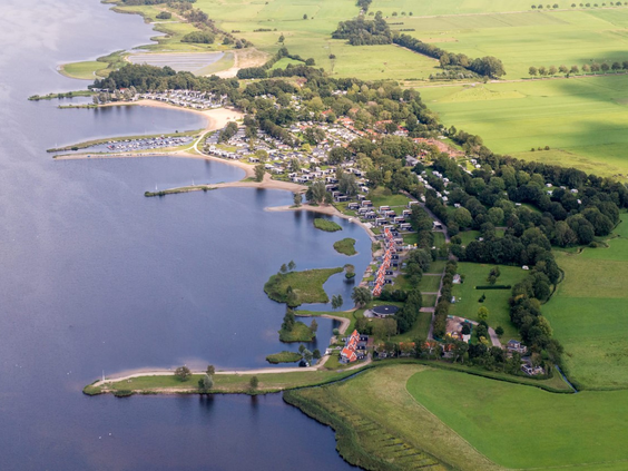 Indrukwekkende luchtfoto van Vakantiepark Bad Hoophuizen, die de unieke ligging direct aan de uitgestrekte kust van het Veluwemeer laat zien.