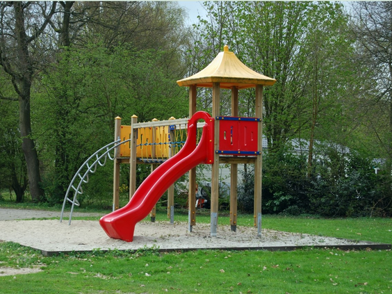Een vrolijke, kleurrijke speeltoren met een rode glijbaan en een klimrek in de buitenspeeltuin van Bad Hoophuizen.