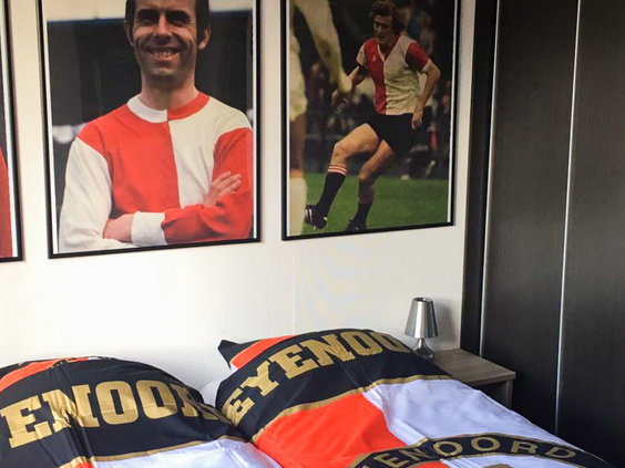 De slaapkamer van de Feyenoord Lodge met foto's van helden aan de muur en een dekbedovertrek met het Feyenoord-logo.