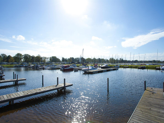 De zonnige jachthaven van Vakantiepark Bad Hoophuizen, met zeilbootjes en motorjachten aangemeerd aan de steigers in het Veluwemeer.