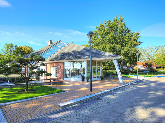 Het moderne centrale gebouw met de receptie en horeca van Vakantiepark Bad Hoophuizen, omgeven door groen.