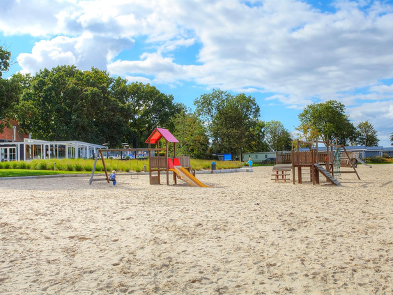 Een leuke speeltuin met een glijbaan, schommels en klimtoestellen, gelegen in het zand van het strand bij Bad Hoophuizen.