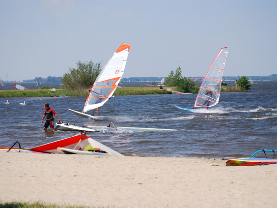 Windsurfers in actie op het water van het Veluwemeer bij Vakantiepark Bad Hoophuizen, een ideale locatie voor watersport.