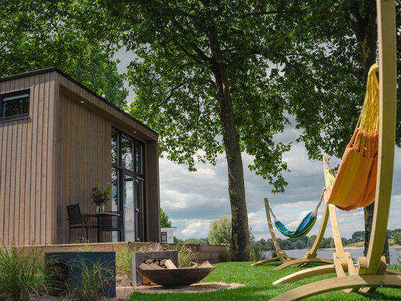 Een relaxte setting met een hangmat en vuurkorf in de tuin van een vakantiehuisje direct aan het water op Bad Nederrijn.
