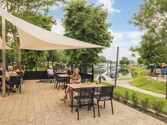 Zonnig horecaterras op Vakantiepark Bad Nederrijn, waar gasten genieten van het uitzicht op de jachthaven en het water.