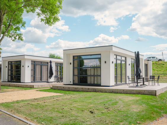 Twee moderne, witte chalets met een terras en een groot grasveld ervoor, gelegen op Vakantiepark Bad Nederrijn.
