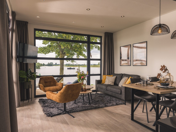 Woonkamer van een chalet met grote ramen die een prachtig uitzicht bieden op de Nederrijn bij Vakantiepark Bad Nederrijn.