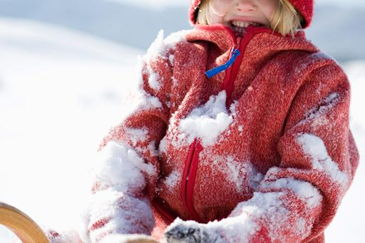Een kind in een rode jas zit vol met sneeuw na het spelen en rollen in de diepe sneeuw tijdens een wintervakantie.