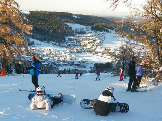 Een groep skiërs en snowboarders rust uit op een brede piste met een adembenemend uitzicht over het besneeuwde dal van Willingen.
