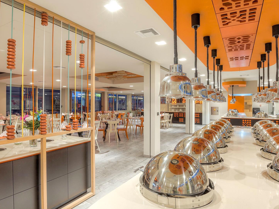 Het moderne buffetrestaurant van Blue Lagoon Resort met een frisse, oranje inrichting en rijen zilveren schalen met warme gerechten.
