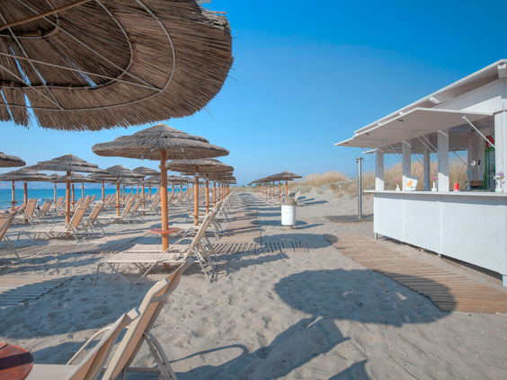Het privé zandstrand van Blue Lagoon Resort op Kos, met rijen ligbedden, rieten parasols en een witte strandbar.