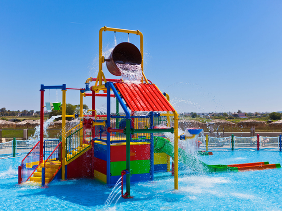 Een kleurrijke waterspeeltuin voor kleine kinderen bij Blue Lagoon Resort, met glijbanen en een grote omkiepende emmer die voor een waterval zorgt.